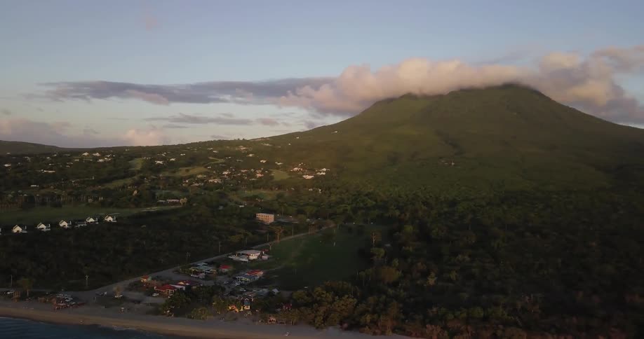 The town is right by a large green hill with clouds on top