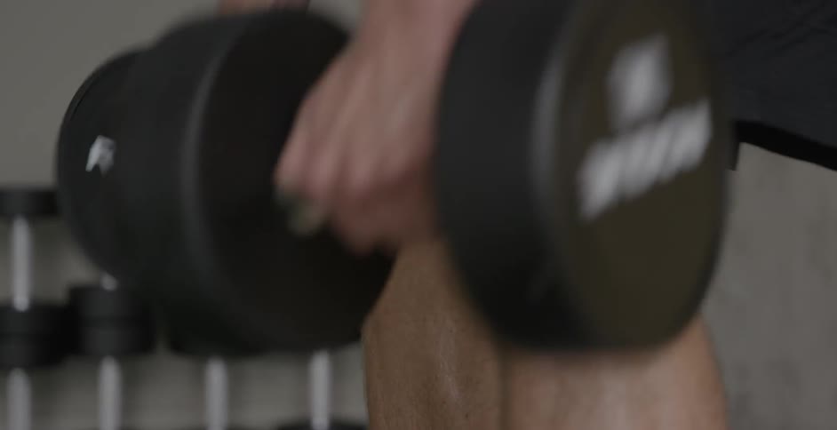 A man is lifting dumbbells inside a gym during the day