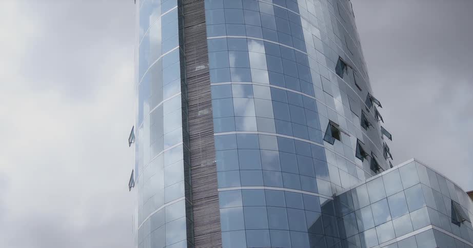The glass windows of a skyscraper are reflecting the clouds in the sky during the day