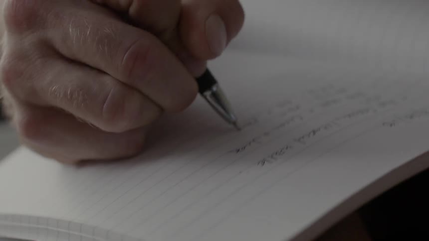 A man is writing words in a notebook during the day