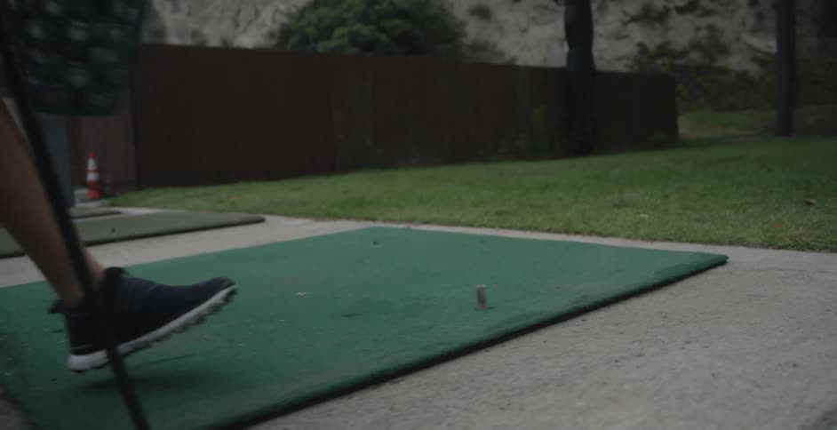 A woman is placing her bag and a bucket of golf balls down on a driving range