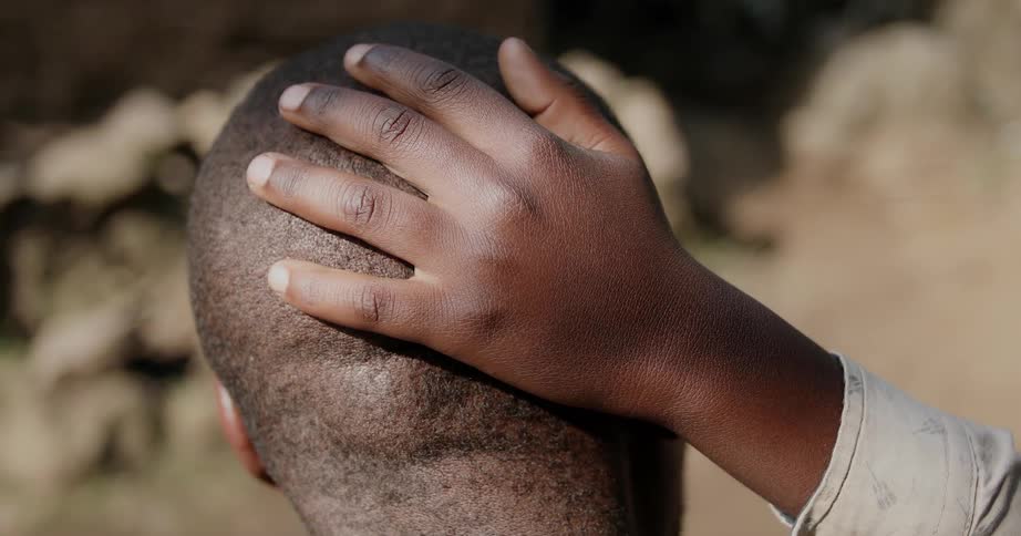 A boy is patting a man's head as he talks to him outside in daylight