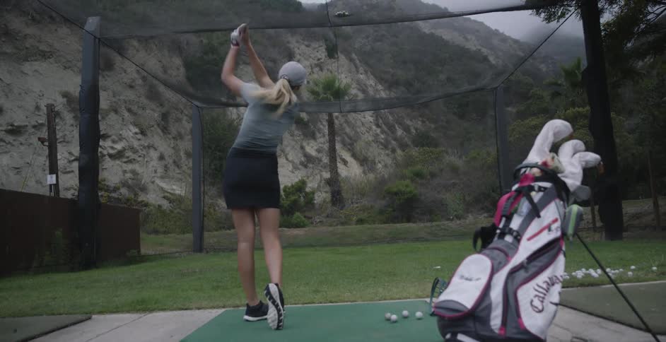 Woman practices hitting golf balls in an enclosed area