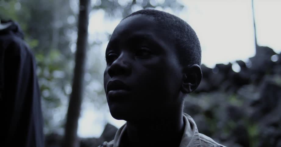 A boy stands outside near trees