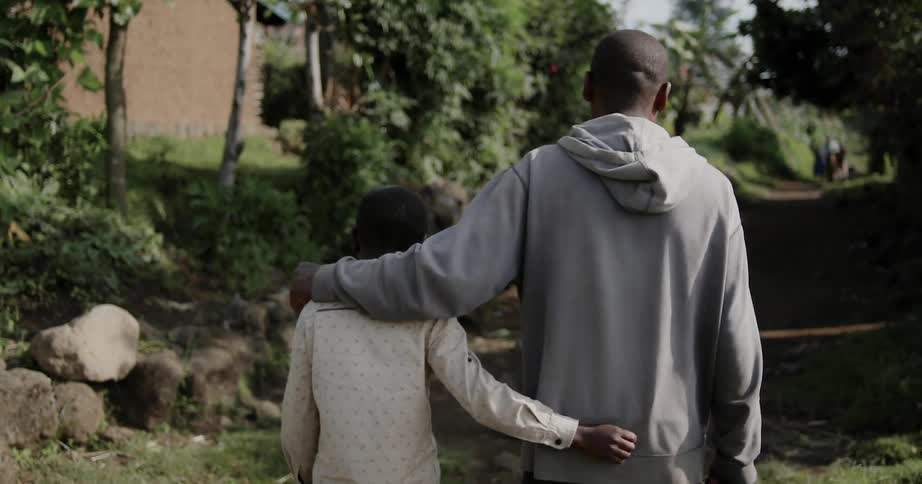 A man and boy are walking through a village in the jungle