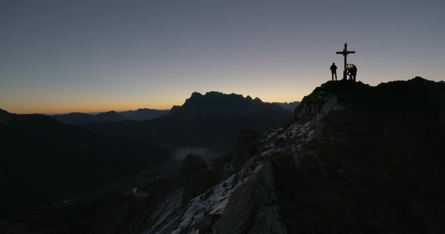 Climbers stand on a peak where a cross has been raised