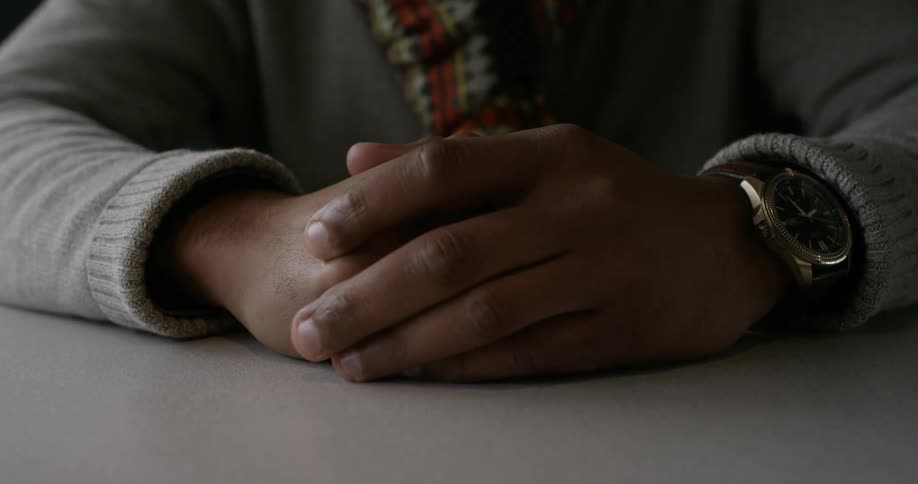 A man sits with his hands in front of him