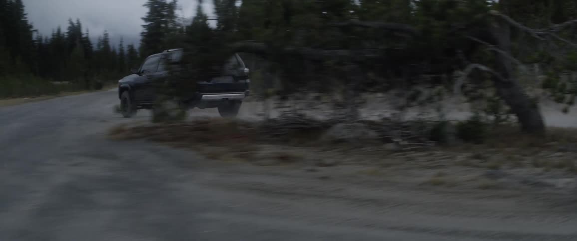 An suv is driving fast on a rural dirt road at dusk