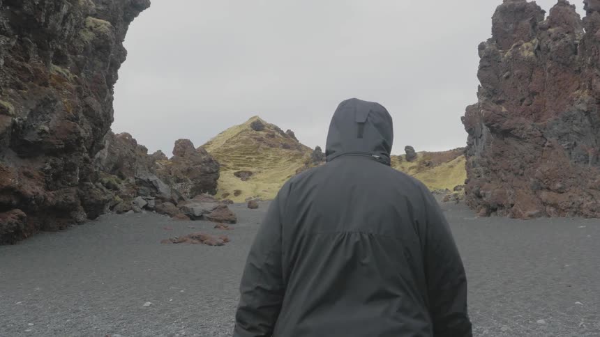 Man walking on some sand between rock formations on a cloudy day