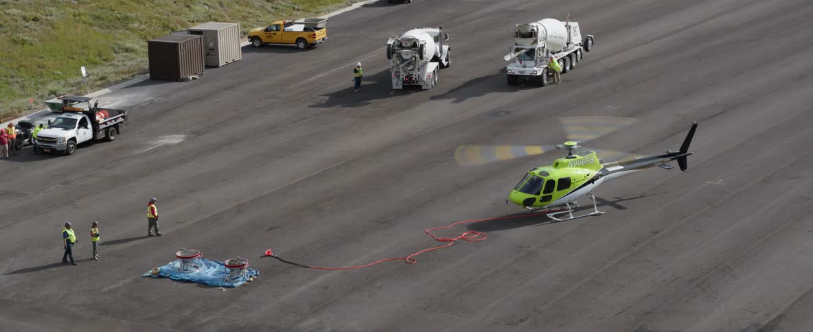 A helicopter's rotors are spinning as it sits on a tarmac during the day