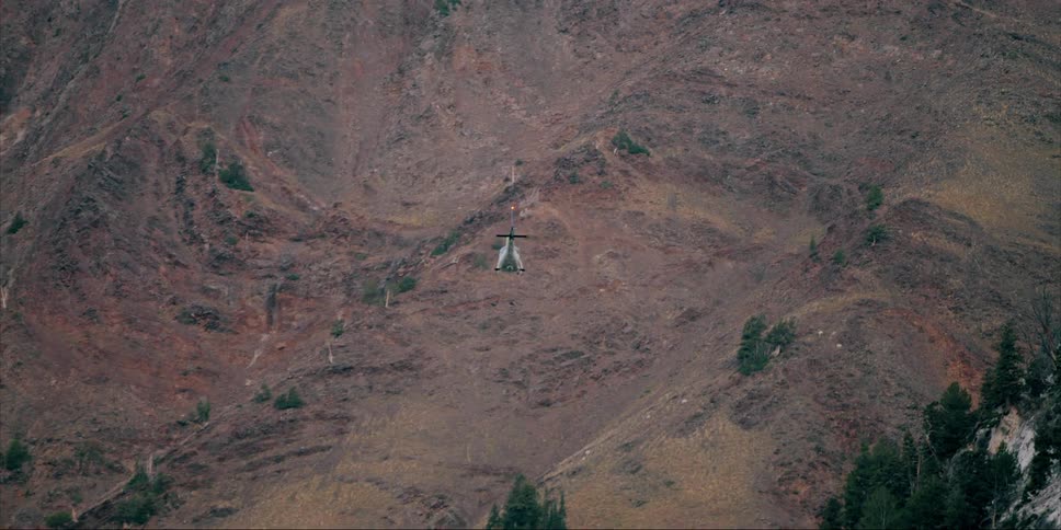 A helicopter is flying towards mountains at dusk