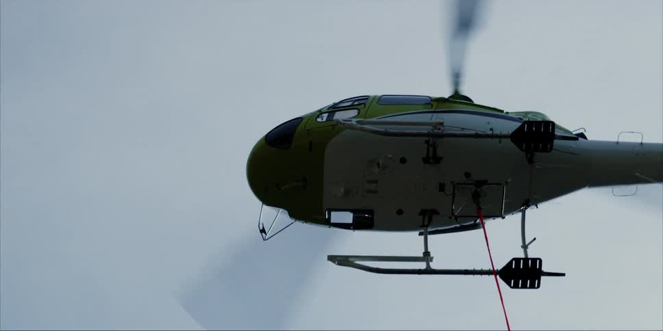 A helicopter dangling a tether is hovering in the sky in daylight