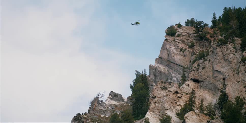A helicopter flies over a rocky mountainside