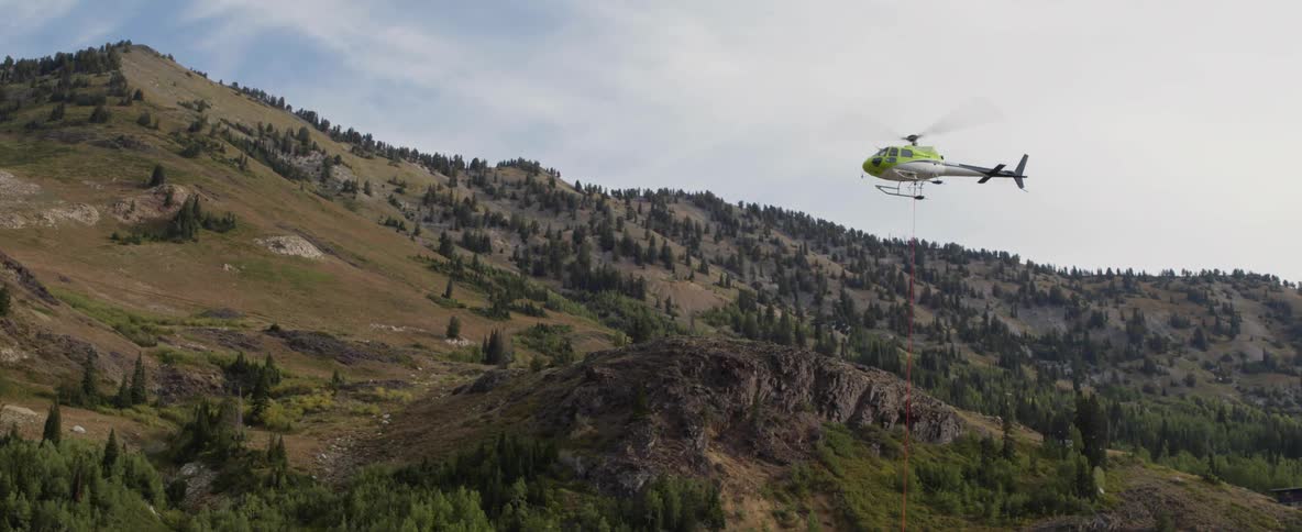 A helicopter dangling a tether is rising into the air during the day