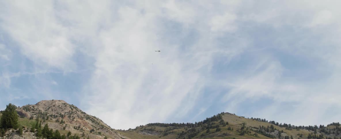 A helicopter is towing a bucket above a mountain ridge during the day