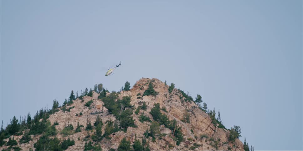 A helicopter flies over a mountain peak