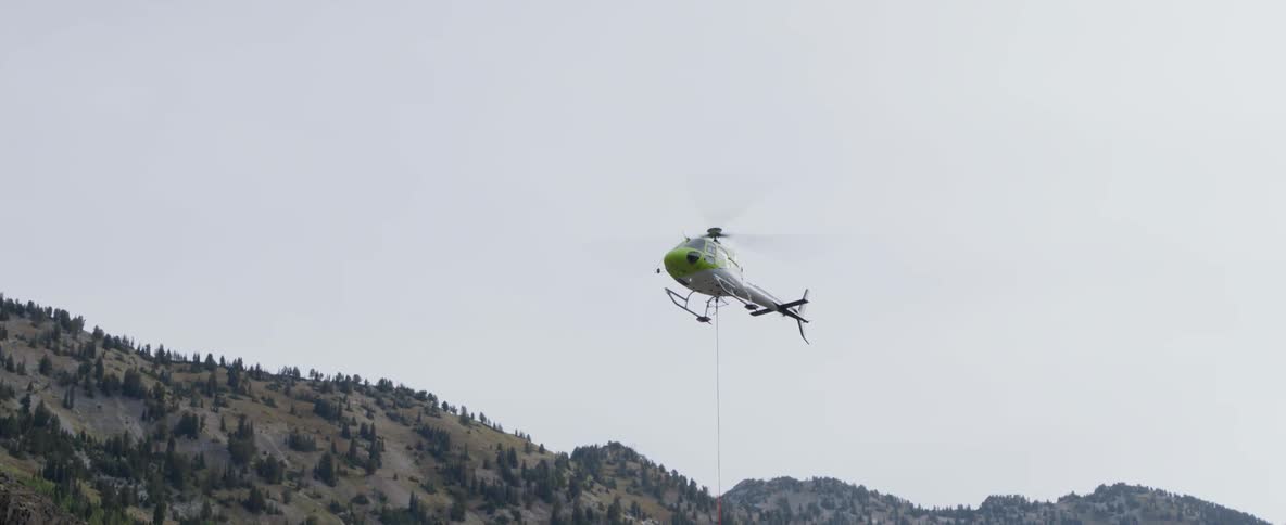 A helicopter is dangling a tether is setting down during the day