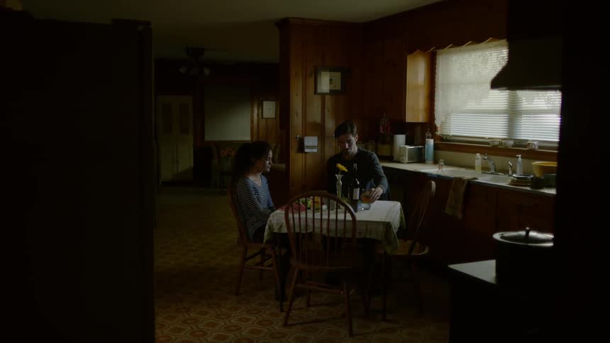 A man sitting at a table with a woman opens a bottle and pours into a glass