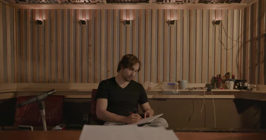 A man sitting in a studio writes on a notebook