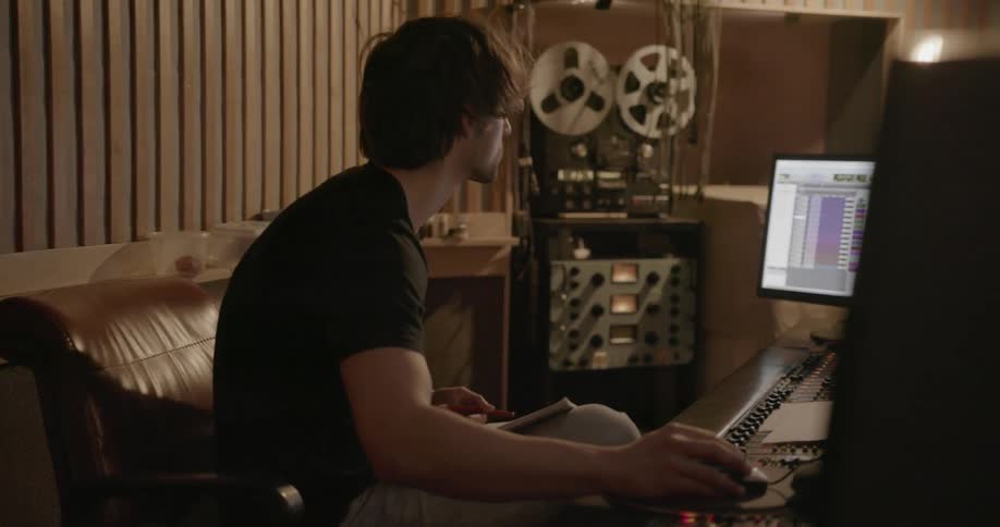 A man sits down at a mixing station in a music studio