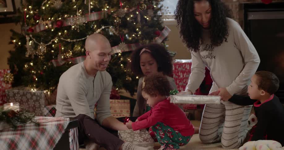 A family opens presents next to a christmas tree