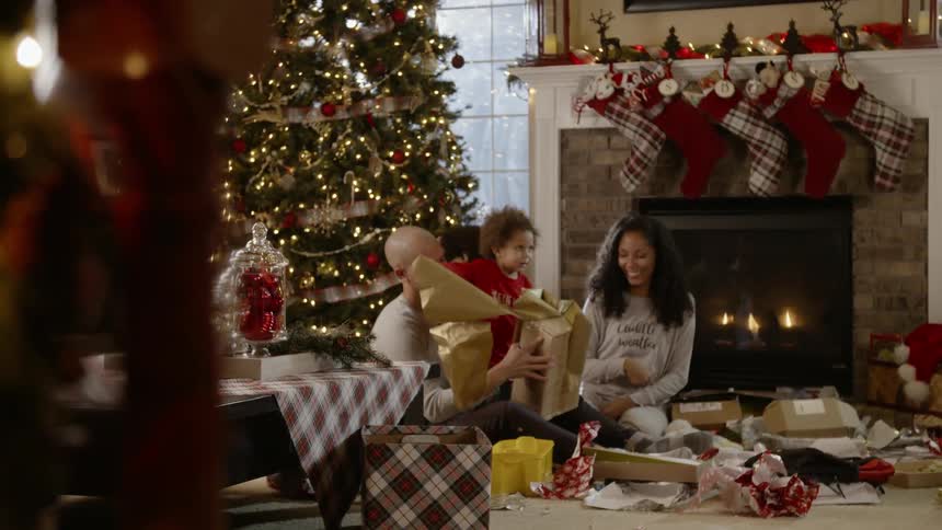 A family are opening christmas presents and throwing the wrapping paper at each other