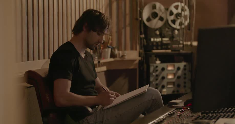 A musician sits down with a notepad in a music studio