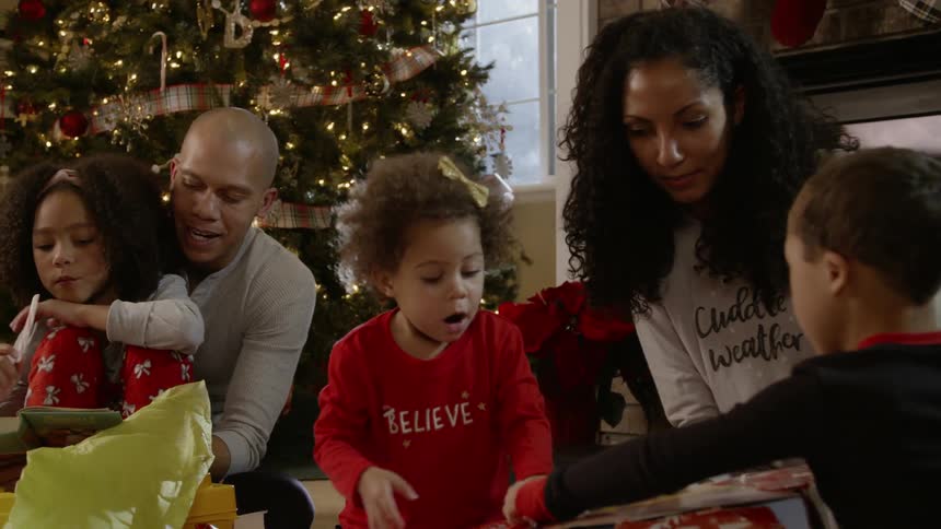 A family opens presents next to a christmas tree