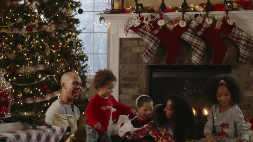 Family unwraps gifts and small child throws wrapping paper in the air