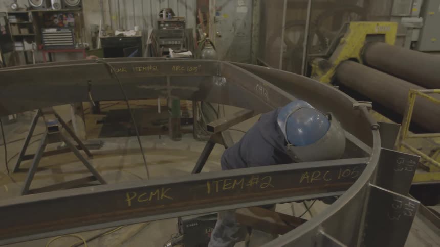 A metalworker works on a steel beam structure inside a workshop