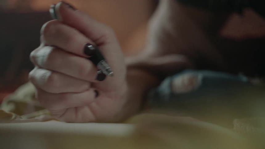 A woman is holding a pen as she writes in a journal