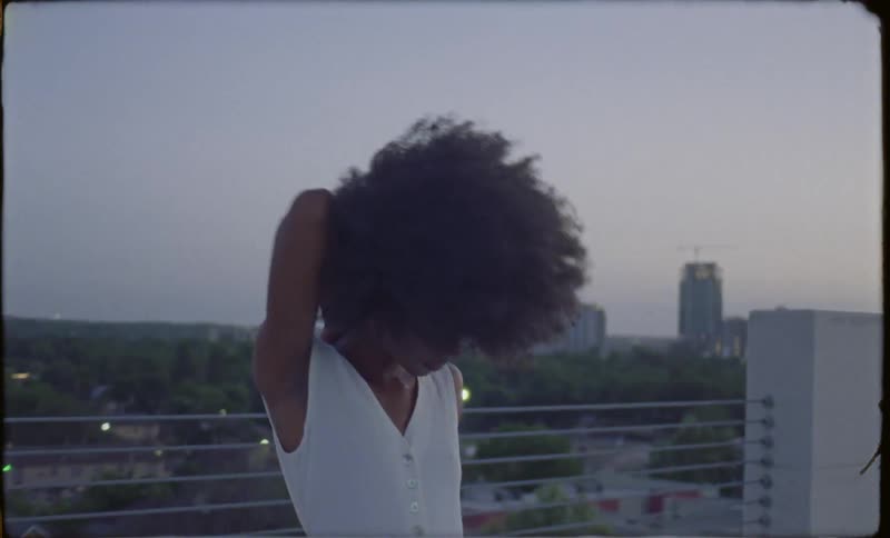 The wind blows a woman's afro as she walks on a roof deck