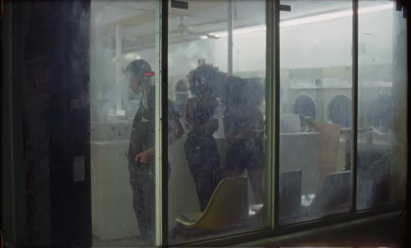 A group of women stand inside a laundromat with dirty windows at night