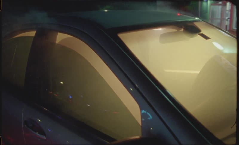 Smoke is pouring from a car a woman is sitting in and combing her hair at night