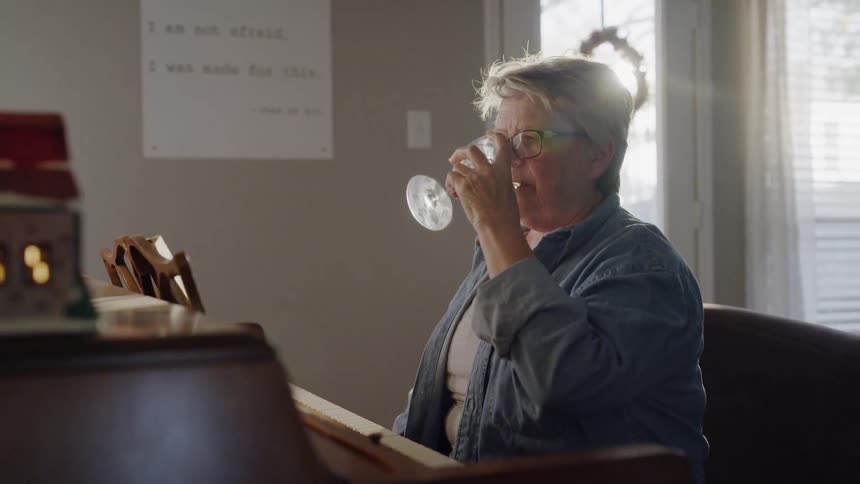 An older woman is playing piano with a glass of wine sitting on top
