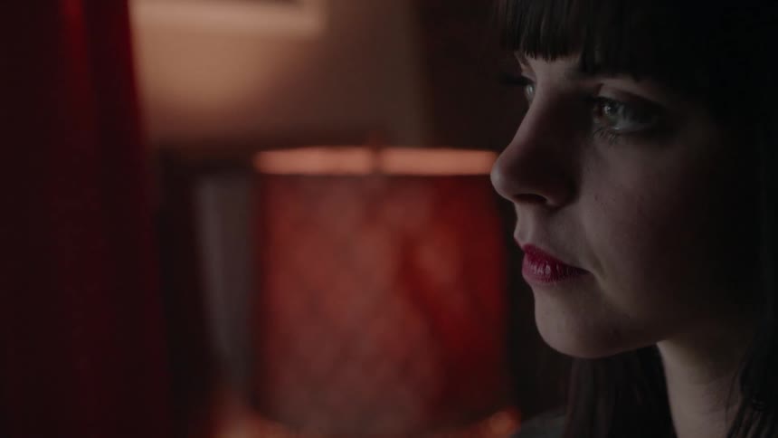 A woman is sitting in a dimly lit room and looks sad