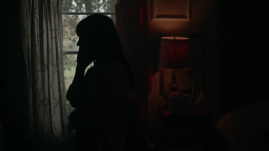 A woman is sitting in a dimly lit room talking on a phone