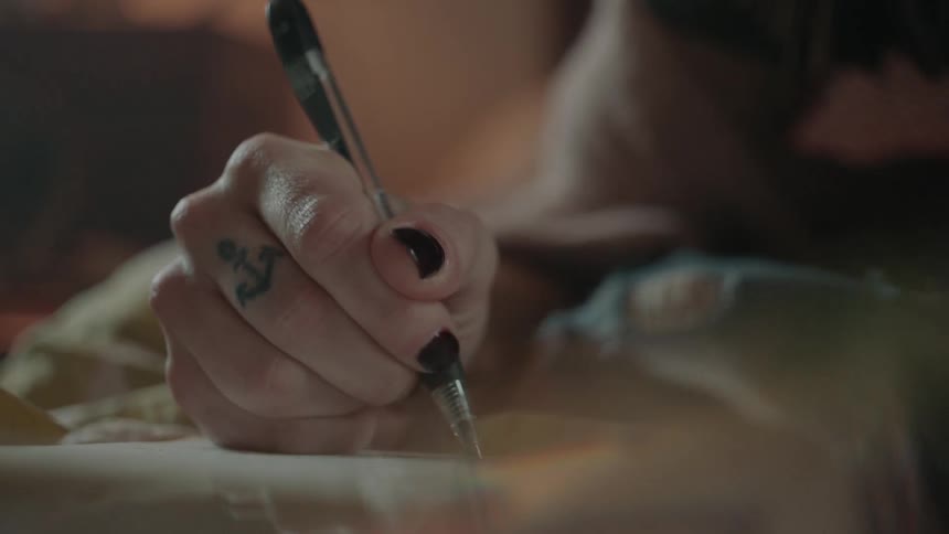 A woman with an anchor tattoo on her finger writes in a notebook
