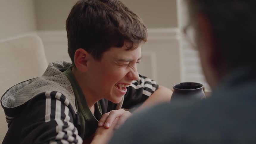 A boy smiles and laughs as he talks to a person at the dining room table