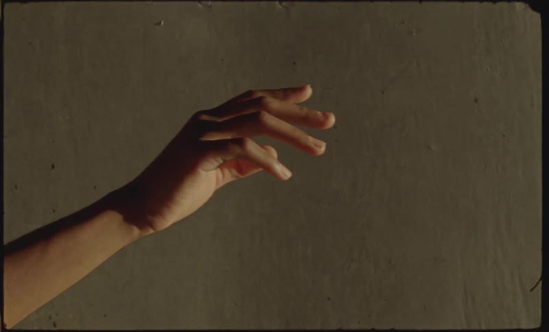 A hand extends in front of a dirty white wall