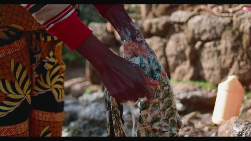 Woman washes clothes near some rocks