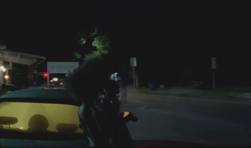 Man and woman stand outside of a car smoking at night