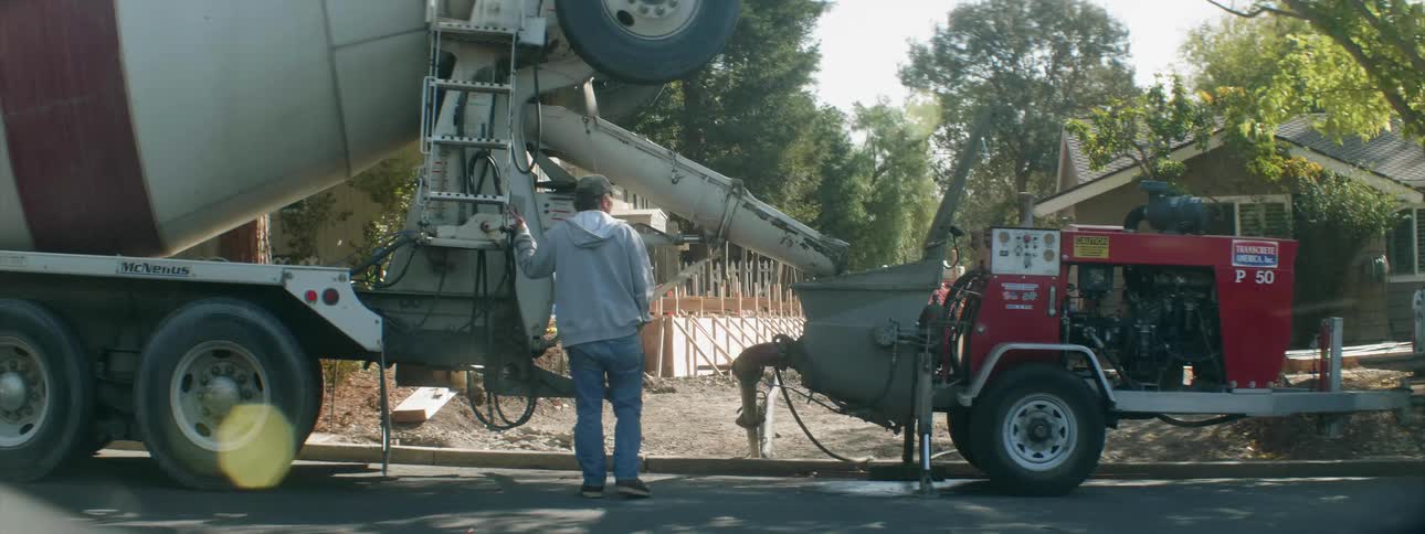 A worker is standing by a cement truck as it pours