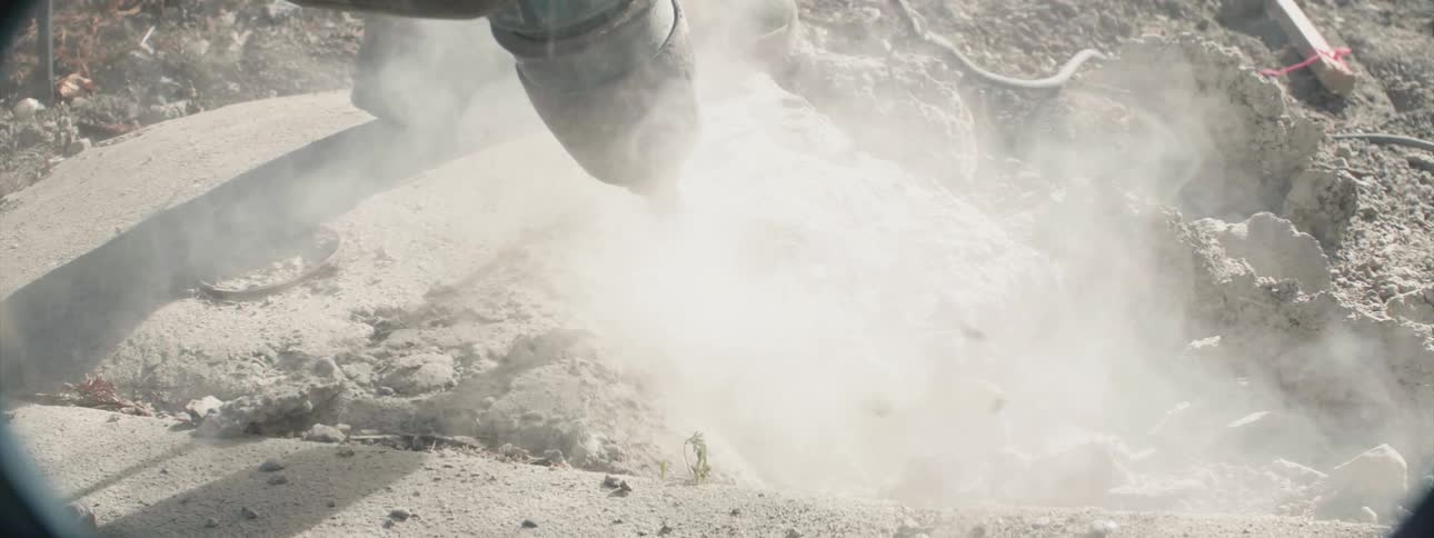 A worker is using a jackhammer to break up concrete during the day
