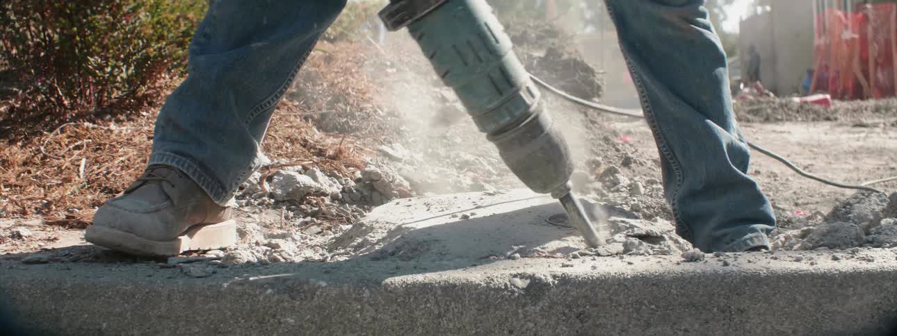 Person uses jackhammer to drill into concrete on a sunny day