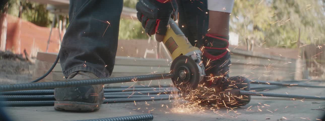 A construction worker is cutting a piece of rebar with a compact circular saw