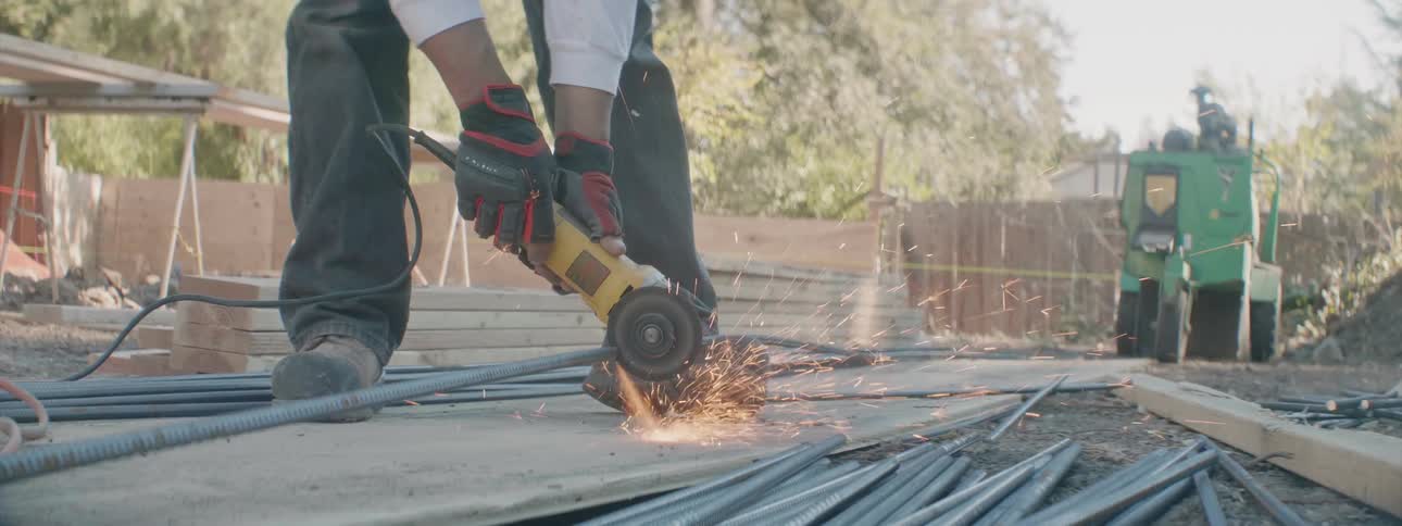 A man is leaning forward cutting rebar poles