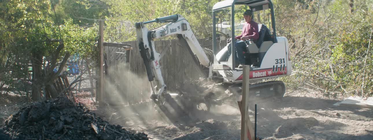 A man uses an excavator to pick up a tree stump