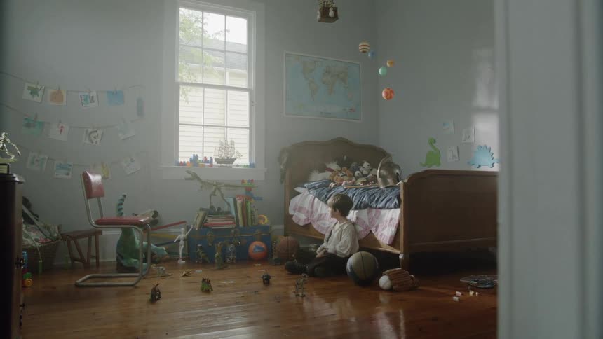 A boy sits in his room looking up at a window during the day