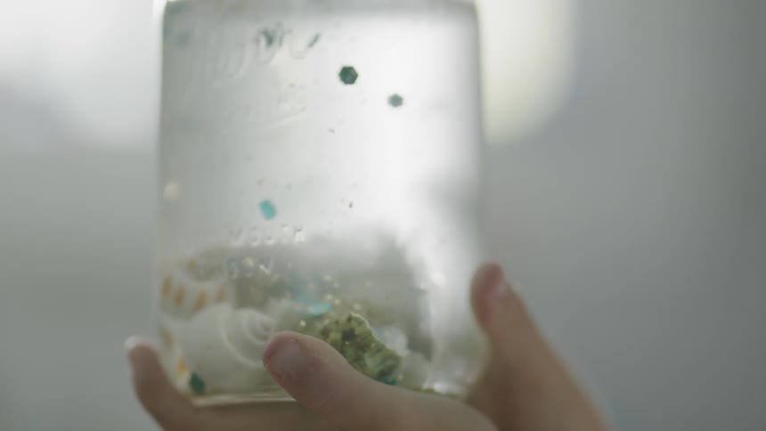 A person holds up a jar with shells in it